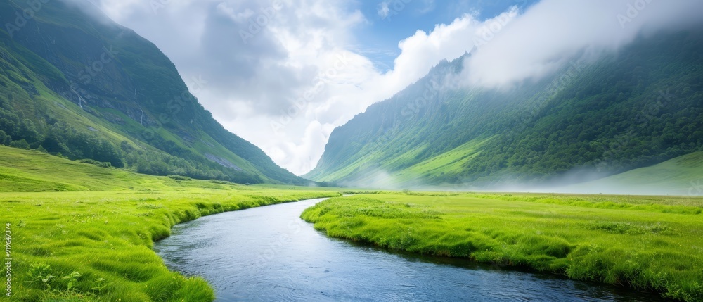 A river runs through a verdant valley, surrounded by lush green grass under a cloudy, blue sky A river runs through a verdant valley, surrounded by lush green grass under a cloudy, blue sky