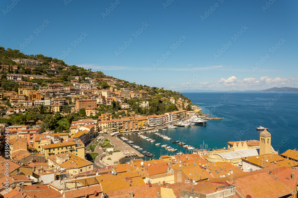 Beautiful panoramic view from above of the bay and the port of Porto Santo Stefano. Municipality of Monte Argentario, Grosseto. Beautiful blue Tyrrhenian sea, clear sky with few clouds. Copy space. Beautiful panoramic view from above of the bay and the port of Porto Santo Stefano. Municipality of Monte Argentario, Grosseto. Beautiful blue Tyrrhenian sea, clear sky with few clouds. Copy space.
