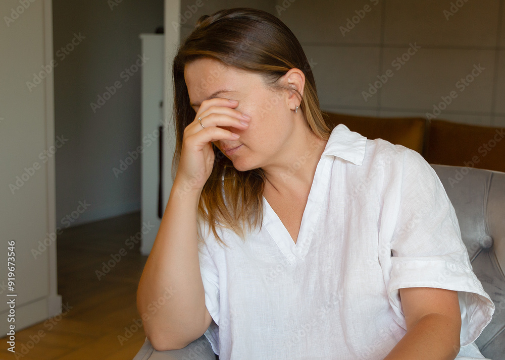 upset woman holding her head with her hands while sitting in a chair in the living room. Fatigue, depression. upset woman holding her head with her hands while sitting in a chair in the living room. Fatigue, depression.