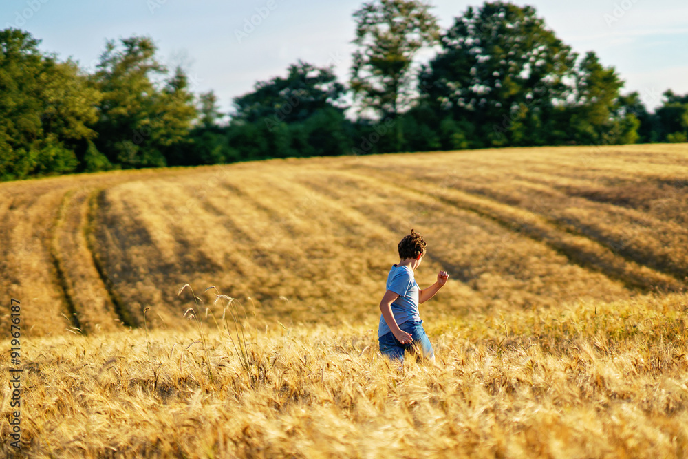 Teenager boy having fun on yellow wheat field in summer on summer day. Active outdoors leisure for family. Happy kid, freedom and vacations concept Teenager boy having fun on yellow wheat field in summer on summer day. Active outdoors leisure for family. Happy kid, freedom and vacations concept