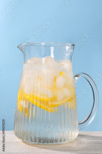 Freshly made lemonade in jug on white wooden table against light blue background