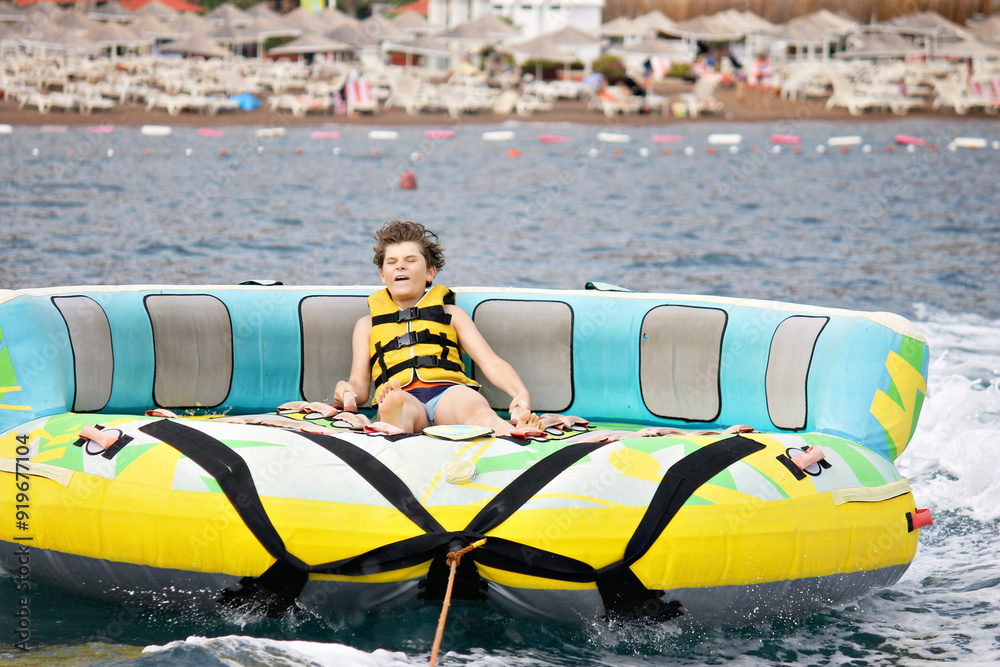 Young boy exudes joy while riding an inflatable tube towed by a boat in ...