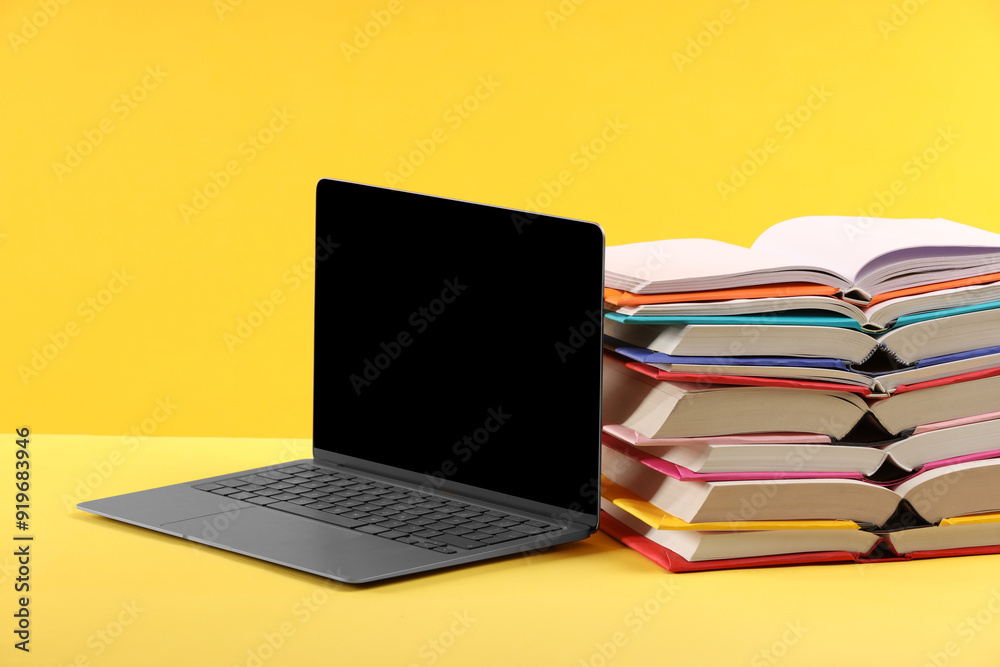 Stack of colorful books and laptop on yellow background Stack of colorful books and laptop on yellow background