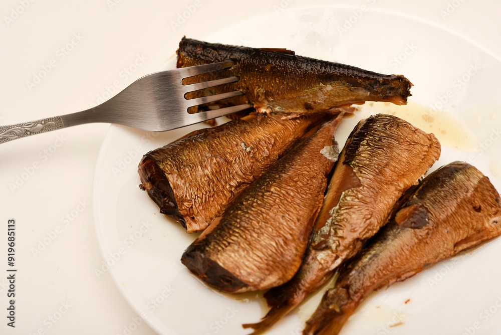 Sprats on a white plate with a fork. Canned fish in oil. Fish appetizer. Sprats on a white plate with a fork. Canned fish in oil. Fish appetizer.