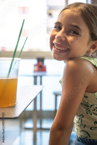 Bambina in bar sorride mentre prende una bevanda fresca