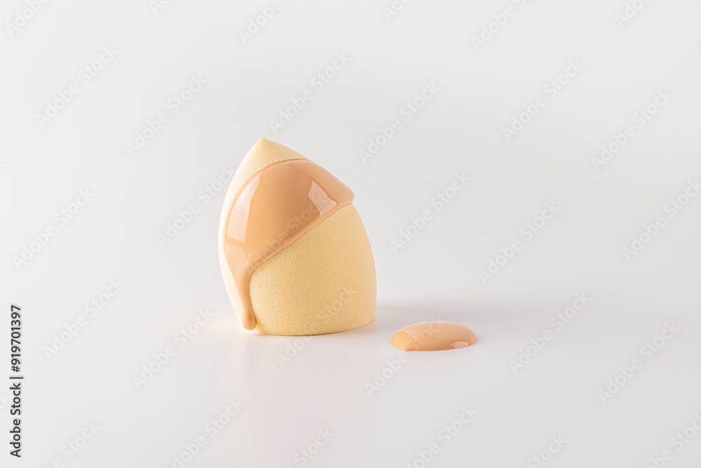 Liquid foundation powder on a beige cosmetic sponge blender in the shape of an egg. The concept of applying makeup face. Front view. white background. Liquid foundation powder on a beige cosmetic sponge blender in the shape of an egg. The concept of applying makeup face. Front view. white background.