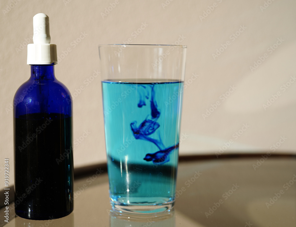 image showing a bottle filled with methylene blue near a glass with water and methylene blue. image showing a bottle filled with methylene blue near a glass with water and methylene blue.