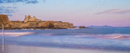 Tantallon Castle, Scotland, on a cliff by the sea at sunrise, with pink sky reflected in the water