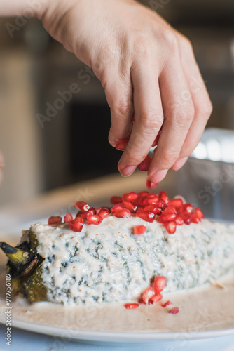 Obraz na plátně Preparation of the famous chiles en Nogada, traditional Mexican food in the month of September, stuffed chile being covered by the nogada which is a cream with walnut and hand adding pomegranate