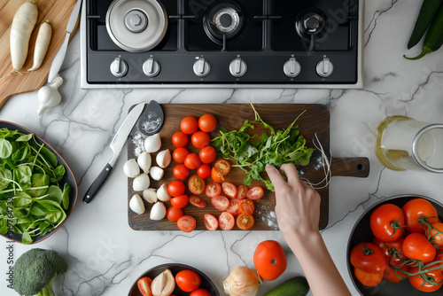 Point-of-view of a person chopping vegetables on a cutting board, with various fresh ingredients and cooking utensils on a kitchen countertop.