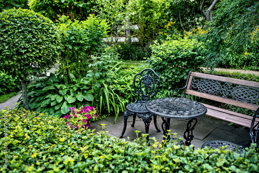 Beautiful carved metal benches, chairs and a table in a luxurious green garden. Beautiful carved metal benches, chairs and a table in a luxurious green garden.