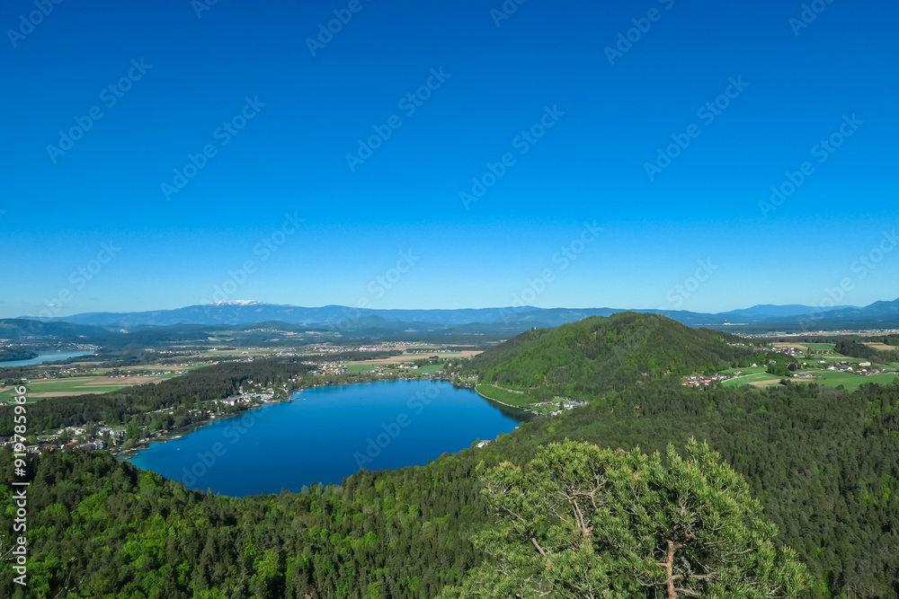 Breathtaking aerial view of a tranquil lake Klopein nestled amidst lush green forest in Carinthia, Austria. Crystal-clear water reflects vibrant blue sky. Rolling hills and mountains in Austrian Alps Breathtaking aerial view of a tranquil lake Klopein nestled amidst lush green forest in Carinthia, Austria. Crystal-clear water reflects vibrant blue sky. Rolling hills and mountains in Austrian Alps