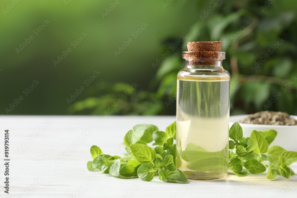 Essential oil in bottle and oregano leaves on white wooden table against blurred green background, closeup. Space for text Essential oil in bottle and oregano leaves on white wooden table against blurred green background, closeup. Space for text