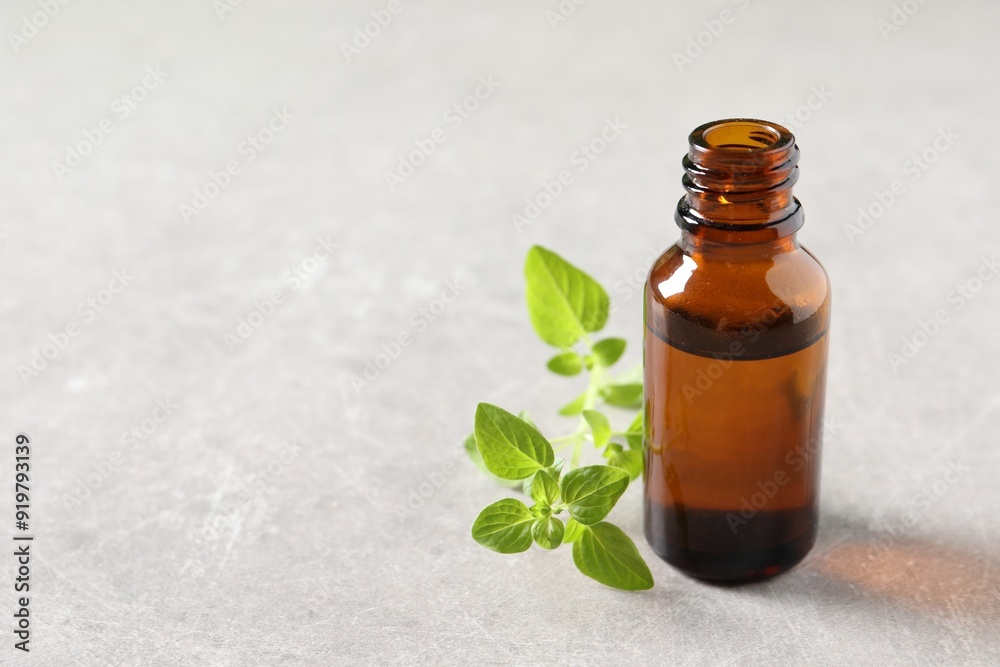 Essential oil in bottle and oregano twigs on light textured table, closeup. Space for text