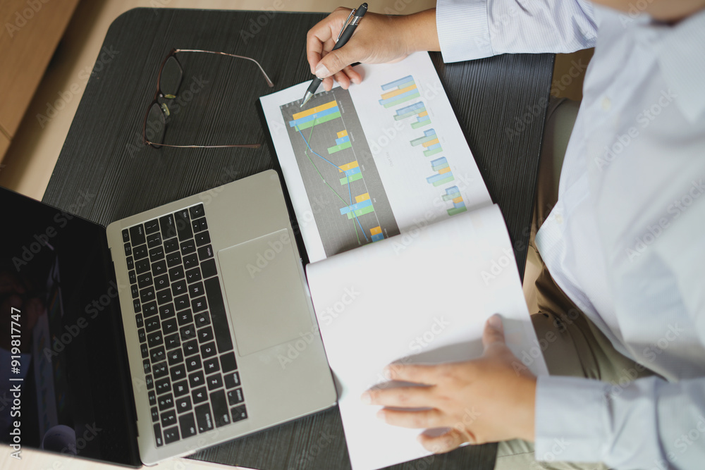 An asian young man accounting manager working at office table, checking the details of the graph and charts of the company total investment before submitting that paper documents to the boss. An asian young man accounting manager working at office table, checking the details of the graph and charts of the company total investment before submitting that paper documents to the boss.