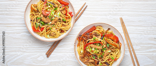 Two bowls with Chow Mein or Lo Mein, traditional Chinese stir fry noodles with meat and vegetables, served with chopsticks top view on rustic white wooden background table. photo