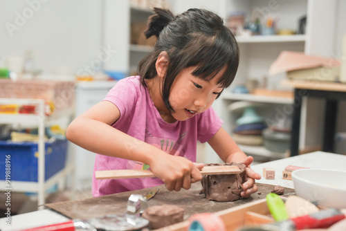 Cuadro en lienzo Young girl intensely focuses on shaping a piece of clay with wooden tool during art class
