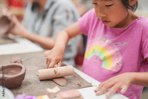 Young girl uses a rolling pin to flatten clay during an art class, Her engagement in the creative process highlights the joy and concentration involved in hands-on learning activities.