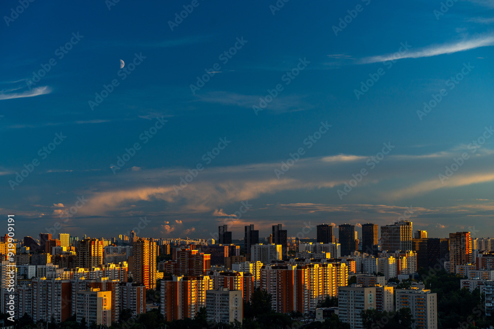 Fototapeta premium A beautiful sunset over a big city, high-rise residential buildings and skyscrapers illuminated by the setting sun against the blue sky. View from above. Moscow, Khovrino district.