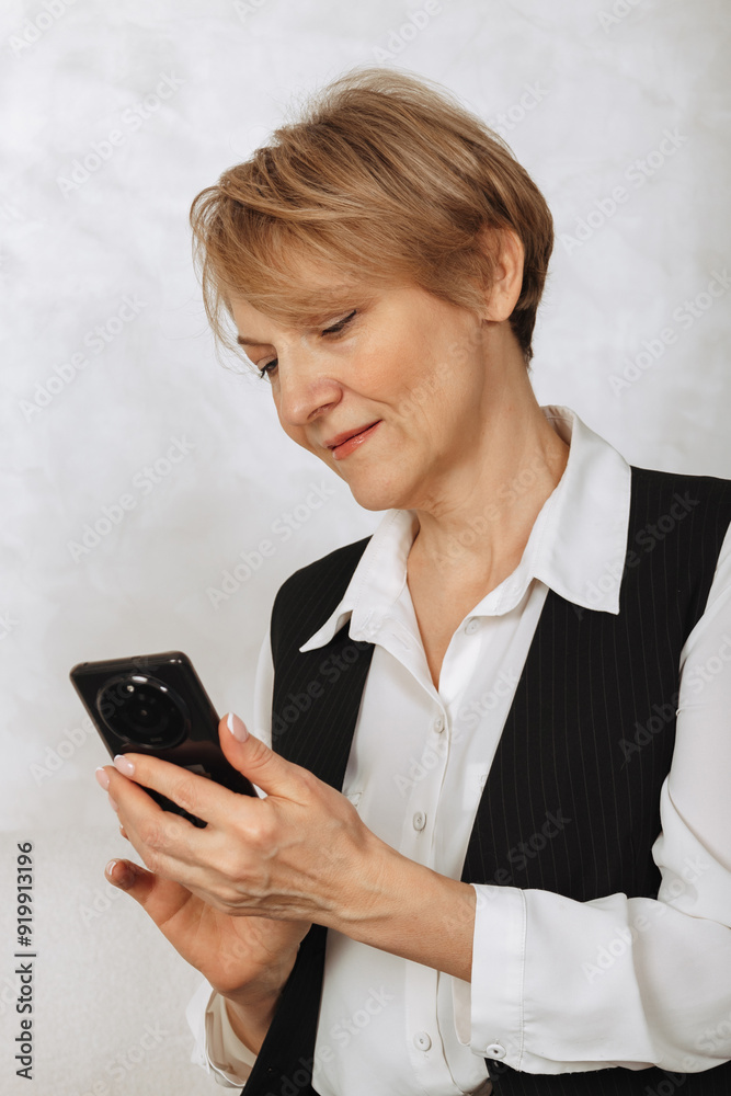 Portrait of business woman. Successful mature woman holding smart phone and reading phone message on light gray background Portrait of business woman. Successful mature woman holding smart phone and reading phone message on light gray background