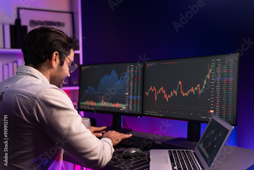 Smart trader businessman concentrating on dynamic stock exchange investment on pc and laptop showing on screen with high profit in searching market at neon light office in dark room night. Surmise.