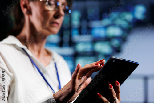 Elderly system administrator using tablet to make sure data remains shielded from security headaches, safeguarding technologically advanced workspace servers against unauthorized access, close up photo