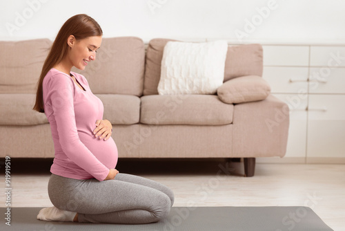 Side View Of Happy Pregnant Woman Embracing Her Belly, Sitting On The Floor, Dreaming About Childbirth