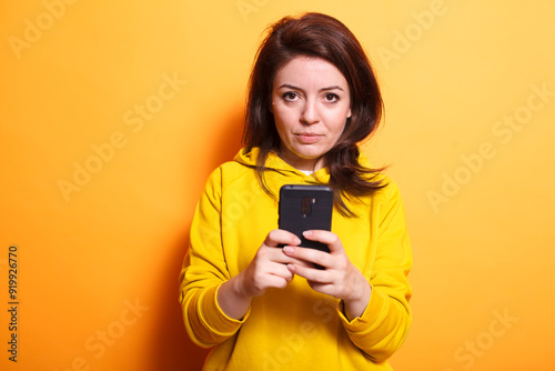 Portrait of woman grasping smartphone on isolated orange background. Stylish and happy, she represents modern communication and technology. Suitable for lifestyle and business concepts.