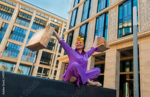 Obraz na płótnie woman with craft shopping bags in the city. The concept of fashionable Consumerism and ecology. An adult Asian woman in a purple suit with red and yellow accents enjoys shopping . a sunny day. w salonie