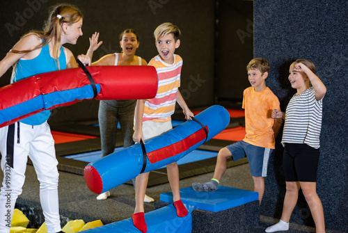 Smiling children having funny wrestling by inflatable logs in indoor amusement park photo