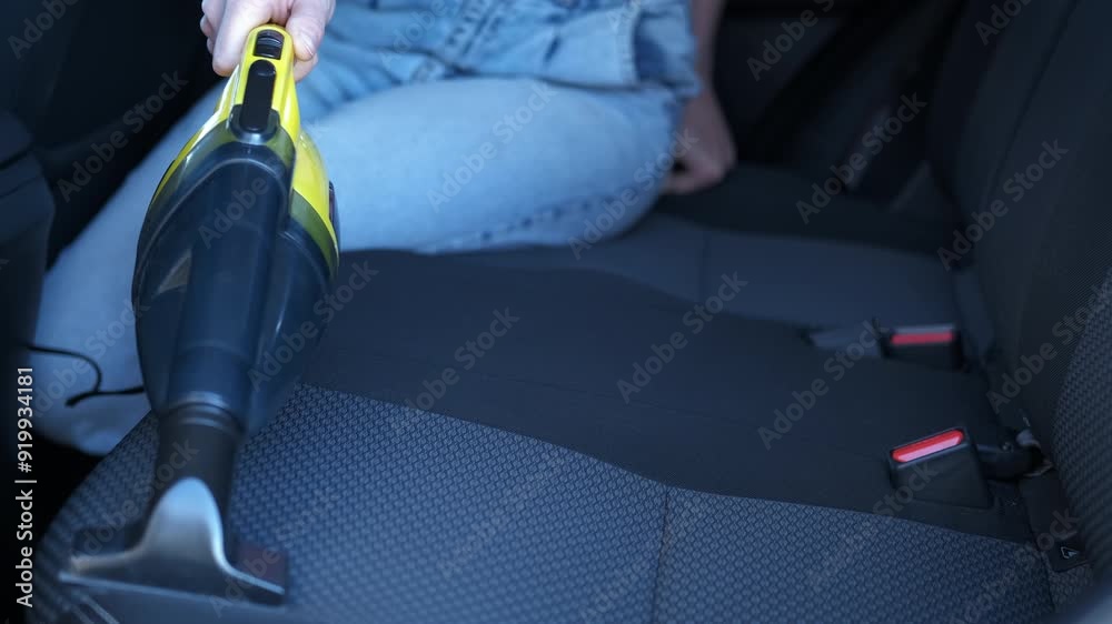 Woman vacuums the seats in car cabin. A woman sits in the car cabin and vacuuming the seats with portable manual device.