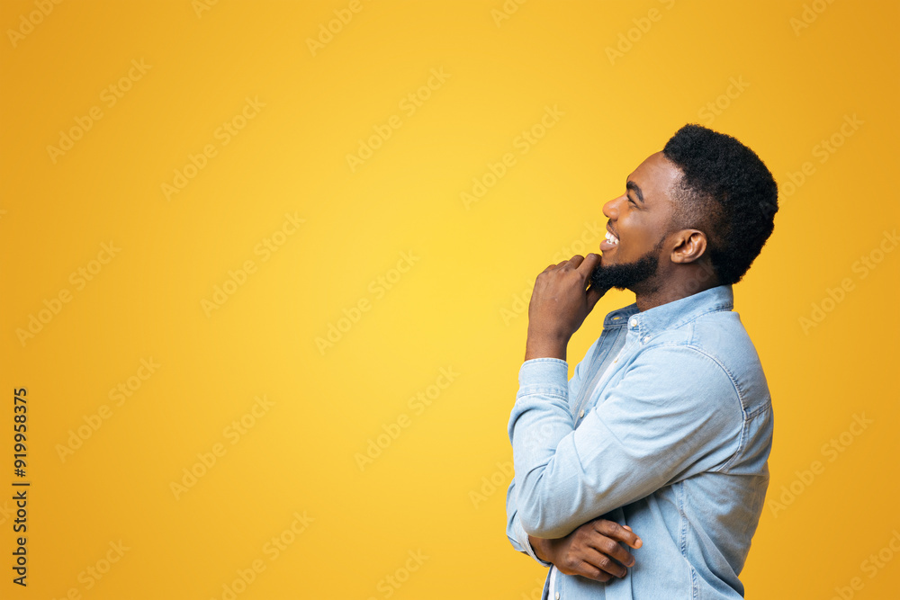 Profile portrait of smiling black guy touching his beard and looking aside at copy space on yellow background Profile portrait of smiling black guy touching his beard and looking aside at copy space on yellow background