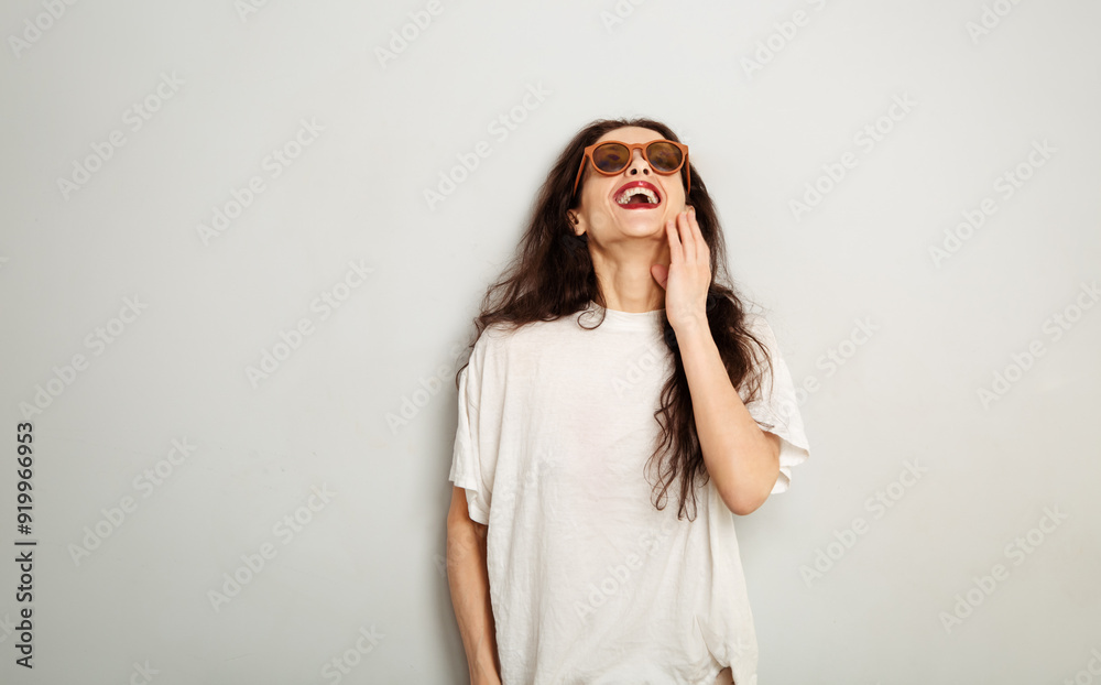 Fun happy natural laughing woman in fashion sunglasses and white t-shirt look up on white wall background with empty copy space. Happy lifestyle Fun happy natural laughing woman in fashion sunglasses and white t-shirt look up on white wall background with empty copy space. Happy lifestyle