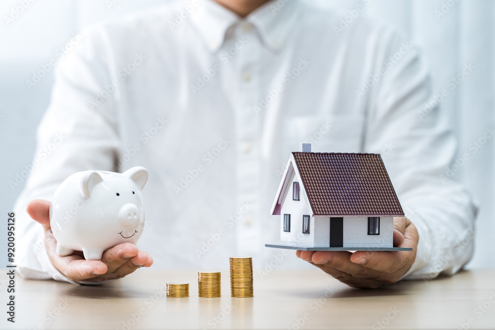 Φωτογραφία Businessman hand hold the piggy bank for saving and stack gold coins with invest and the home model is destination on the desk in the office, Loan and investment the real estate concept