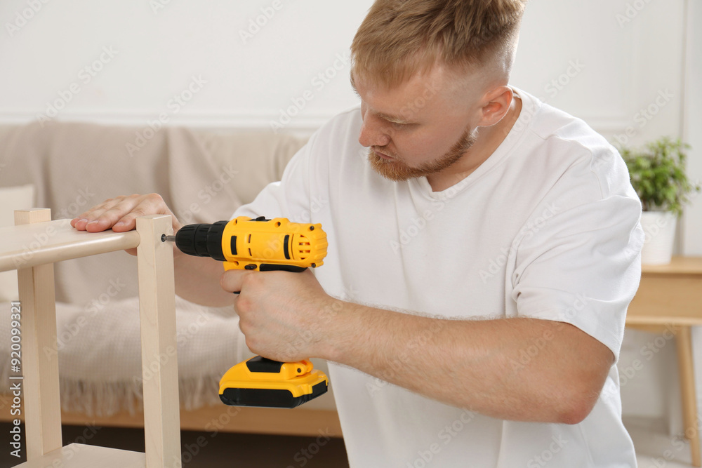 Man with electric screwdriver assembling furniture in room Man with electric screwdriver assembling furniture in room