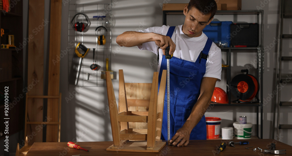 Man using tape measure while repairing wooden stool indoors
