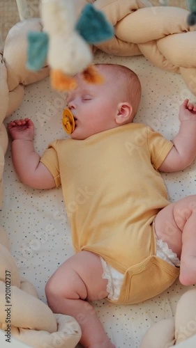 Newborn baby is sleeping in cosy cradle with spinning crib mobile. Handheld high angle shoot with shallow depth of field.