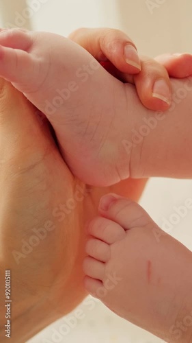 Mother holding in hands foot of newborn baby. Close up of woman gently stroking, touching tiny feet of baby boy. Family care, happy childhood and motherhood.
