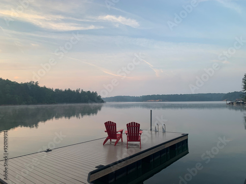 Foto Two red adirondack chairs overlooking the bay at sunrise with the landscape refl