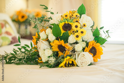 Stunning bridal bouquet with sunflowers and white roses on. bed with bokeh background