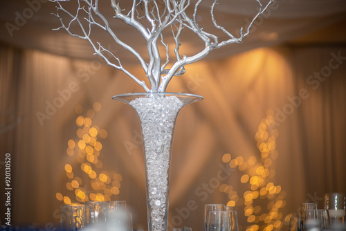 Beautiful glass vase centerpiece filled with glass rocks atwedding reception table in warm reception atmospere