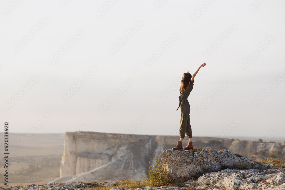 Woman triumphantly raising arms on mountain summit during adventurous travel hike in nature landscape Woman triumphantly raising arms on mountain summit during adventurous travel hike in nature landscape