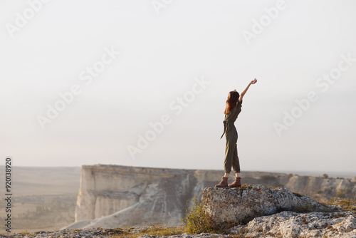 Woman triumphantly raising arms on mountain summit during adventurous travel hike in nature landscape photo