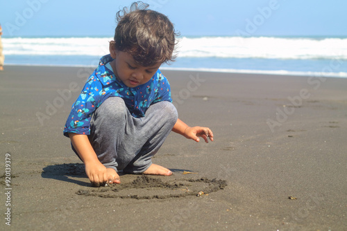 Cute child drawing picture on a sand playing outdoor on summer beach. Boy drawing on sand at seaside. Child drawing sand by imaginary on beach for learning. Kids summer travel and adventure.