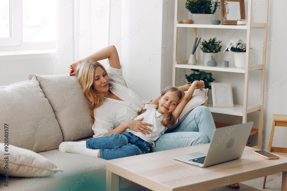 Mother and daughter enjoying quality time together, smiling and engaged with laptop on cozy living room couch Mother and daughter enjoying quality time together, smiling and engaged with laptop on cozy living room couch