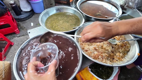 Vietnamese street food, sweet soup is tradition desserts, woman hand scooping che, sugared dishes from deverse bean, banana and coconut milk at outdoor stalls photo