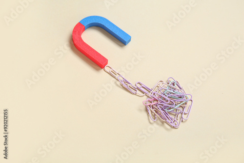Magnet attracting paper clips on beige background