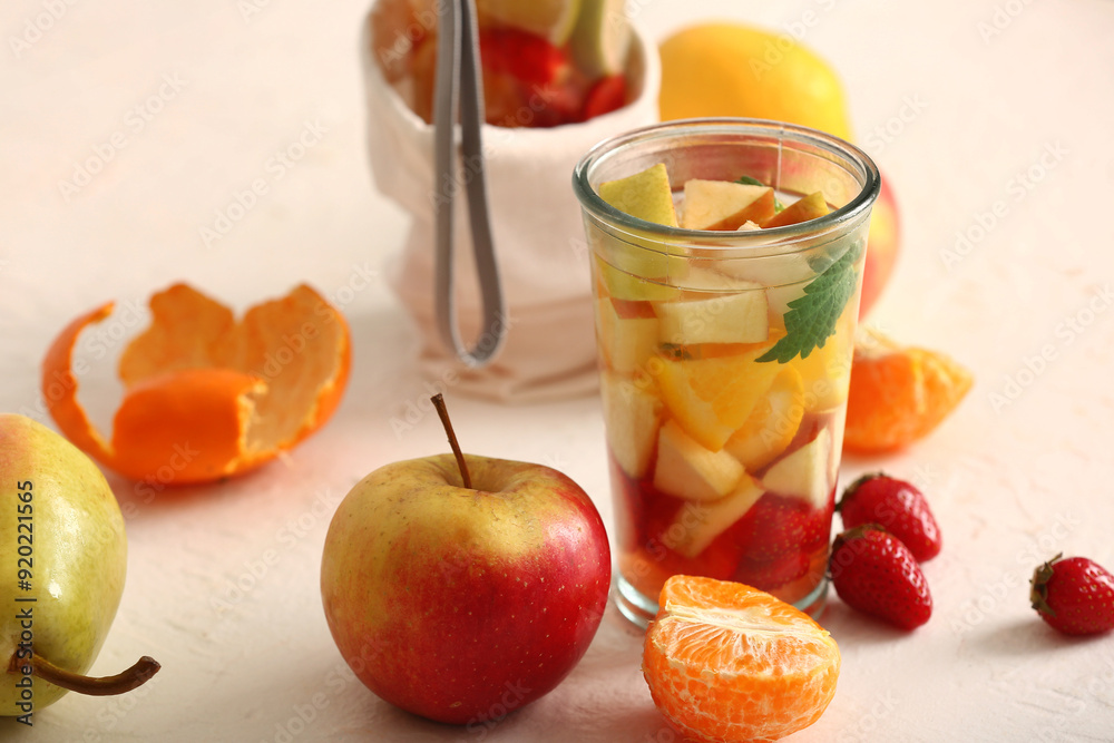 Glass and sports bottle of infused water with different sliced fruits on white table Glass and sports bottle of infused water with different sliced fruits on white table