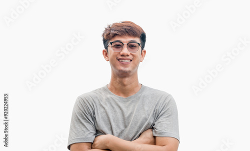 A young Asian man in his 20s wearing glasses and wearing a gray t-shirt stands confidently with his arms crossed over his chest, isolated on a white background. Positive person.