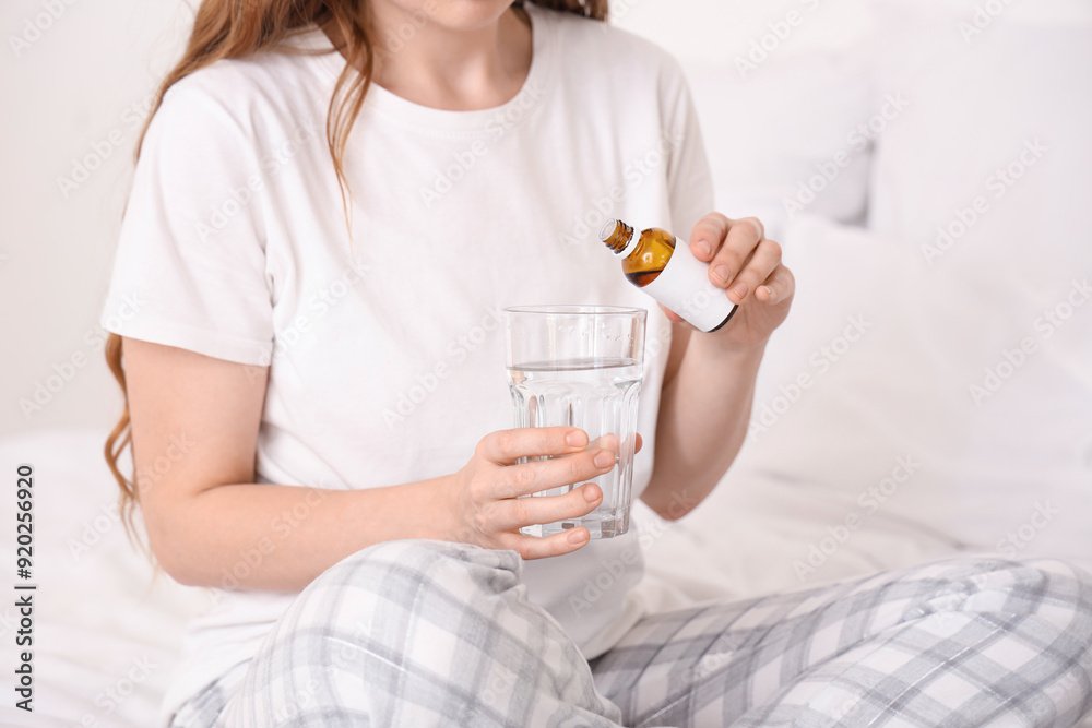 Young woman putting sleeping drops into glass of water in bedroom, closeup Young woman putting sleeping drops into glass of water in bedroom, closeup
